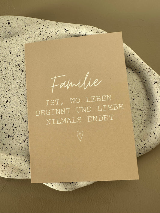 Nahaufnahme der weißen Schrift auf beiger Postkarte mit dem Spruch „Familie ist, wo Leben beginnt und Liebe niemals endet“.