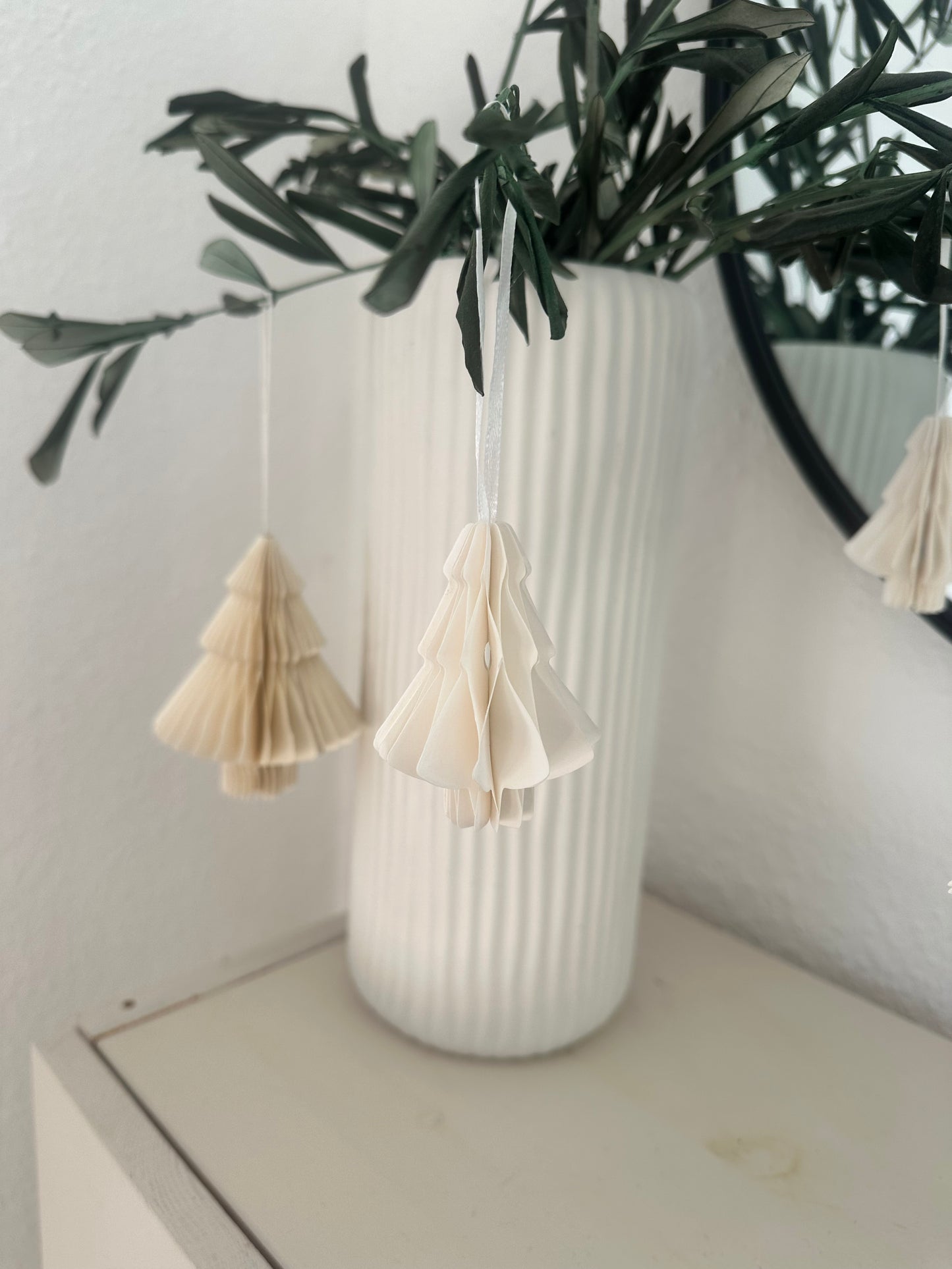 Mehrere weiße Papier-Tannenbäume als moderne Winterdeko hängend an Olivenzweigen