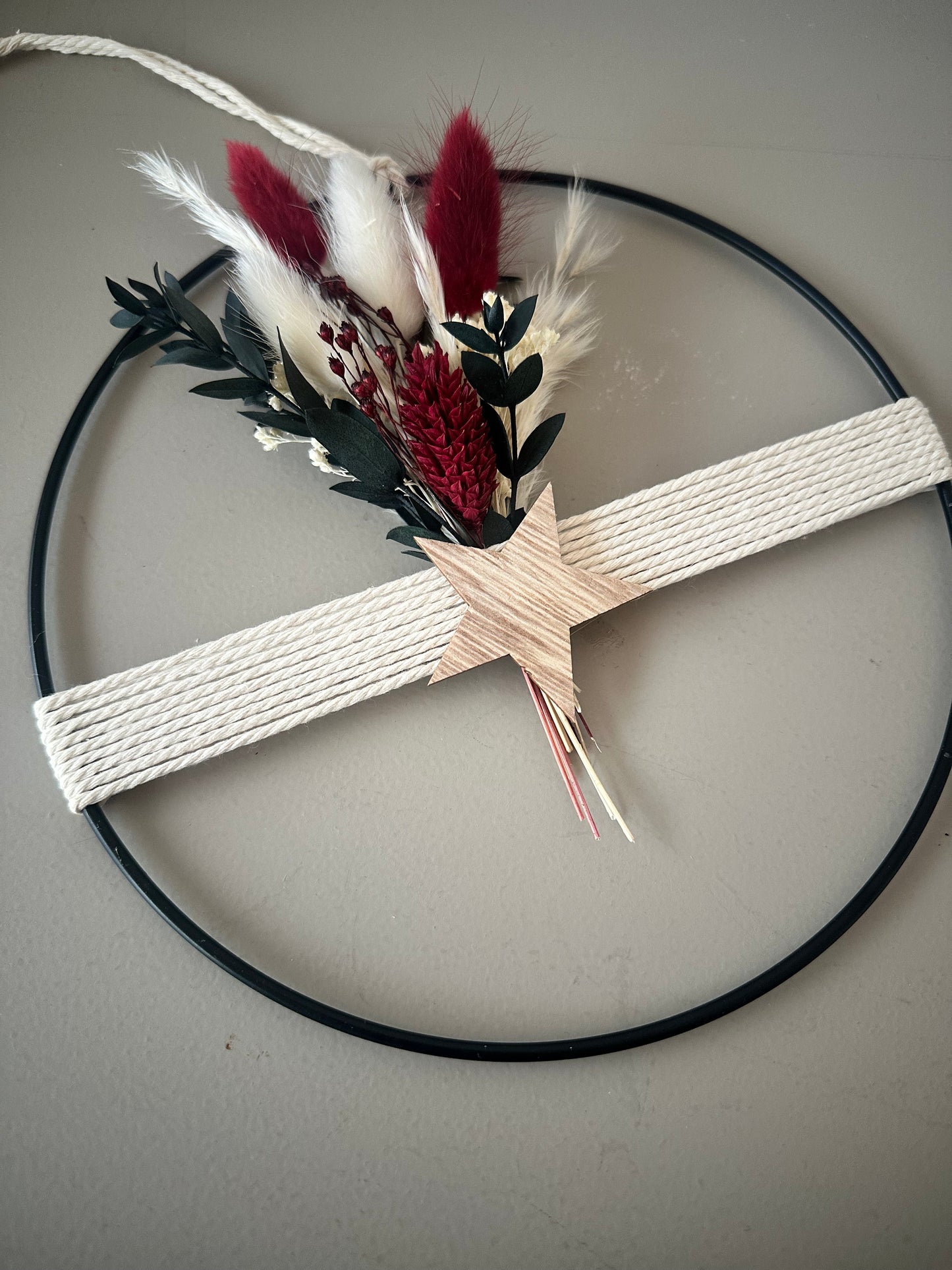 Trockenblumenring mit Garn und Stern als weihnachtliche Wanddekoration