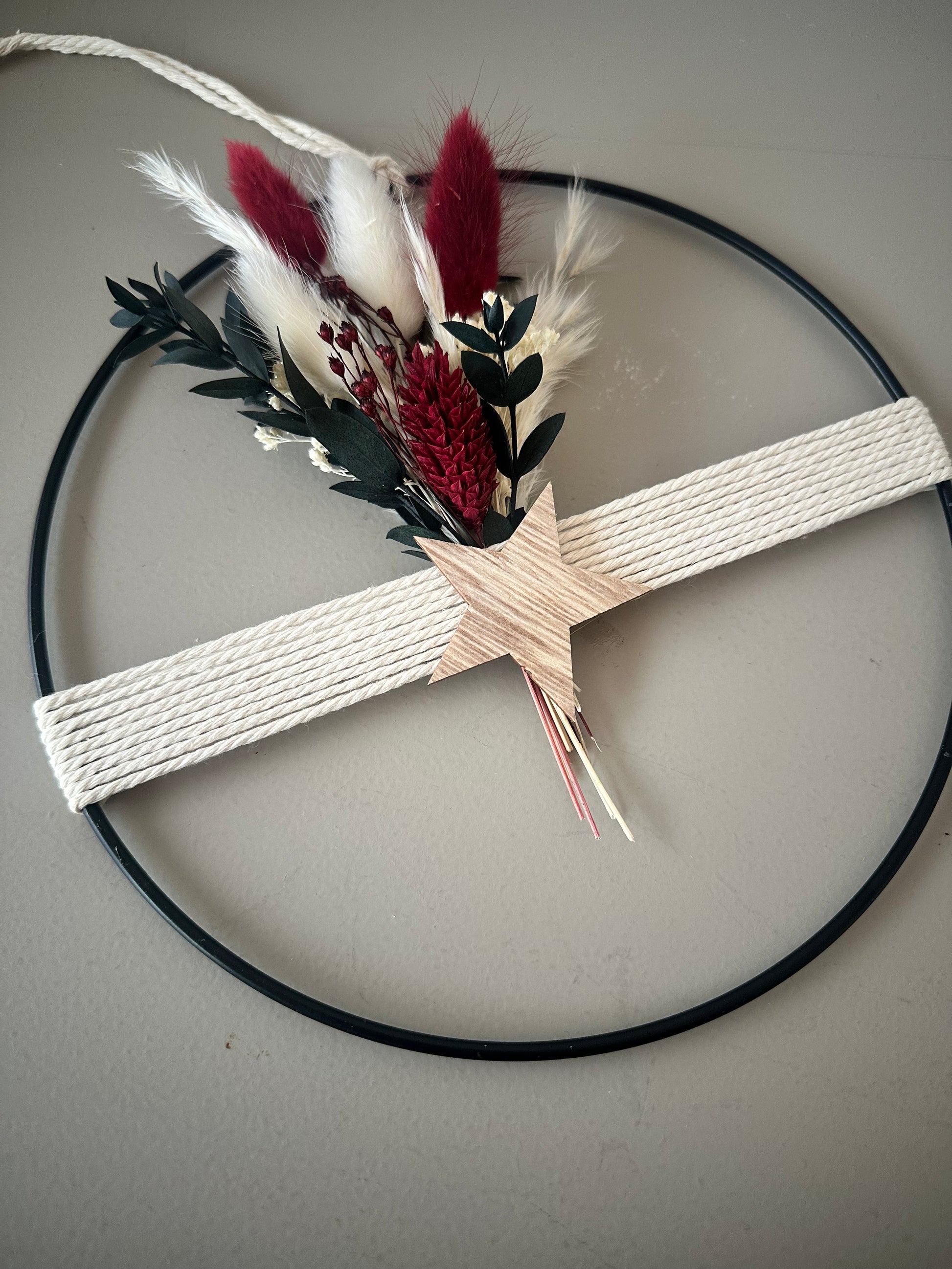 Trockenblumenring mit Garn und Stern als weihnachtliche Wanddekoration