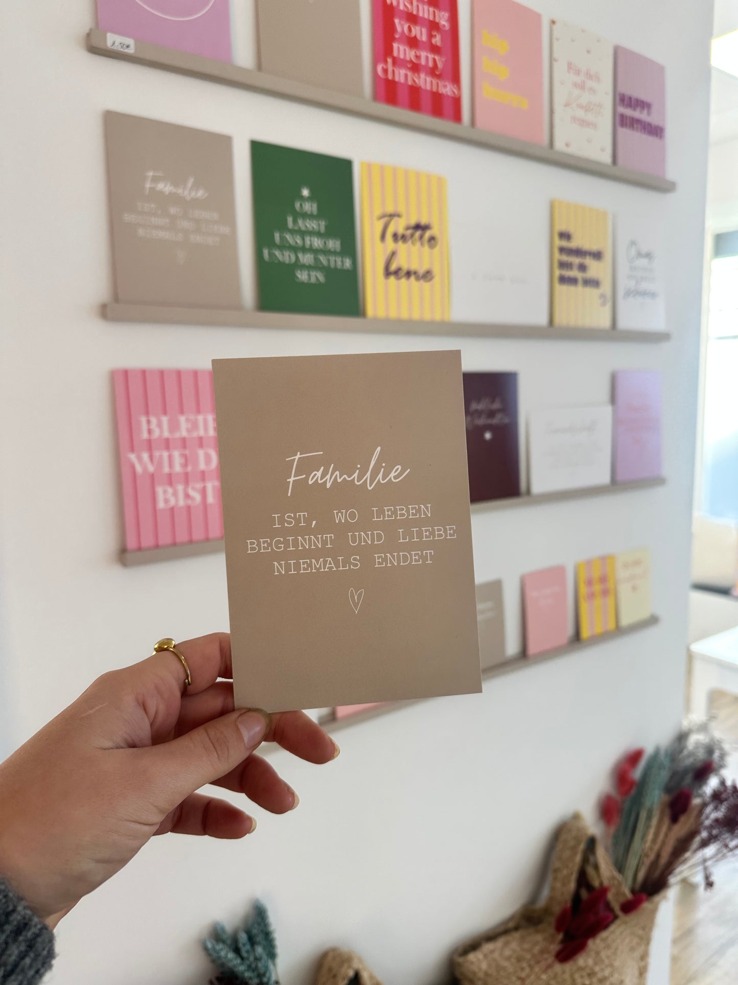 Beige Postkarte mit weißem Schriftzug „Familie ist, wo Leben beginnt und Liebe niemals endet“ auf hellem Hintergrund.