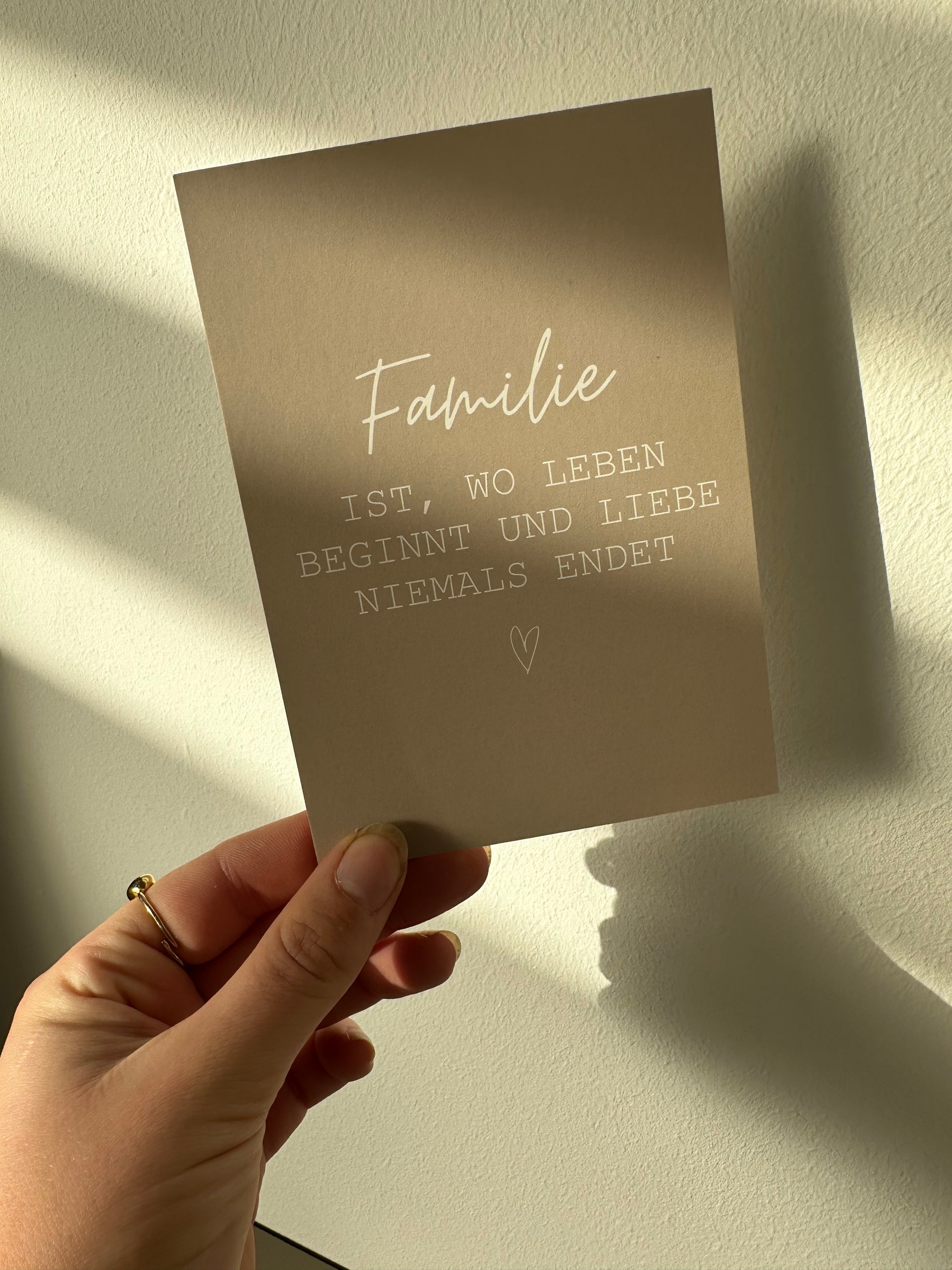 Beige Postkarte mit dem weißen Spruch „Familie ist, wo Leben beginnt und Liebe niemals endet“, liebevoll gestaltet von Lizasliving.