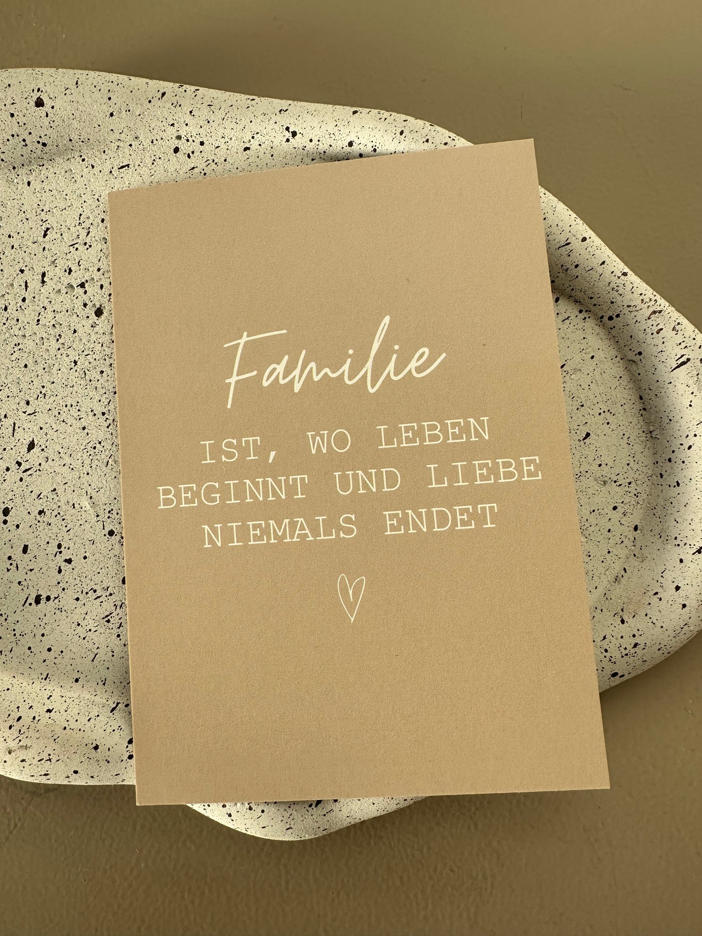 Nahaufnahme der weißen Schrift auf beiger Postkarte mit dem Spruch „Familie ist, wo Leben beginnt und Liebe niemals endet“.